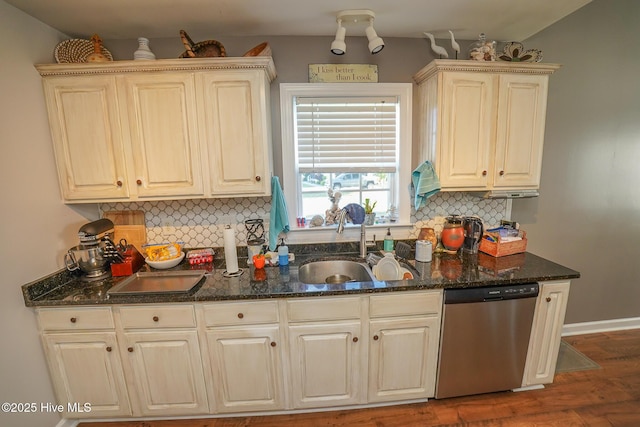 kitchen with wood finished floors, dishwasher, a sink, dark stone countertops, and backsplash