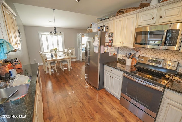 kitchen featuring decorative backsplash, a chandelier, light wood-style floors, stainless steel appliances, and cream cabinetry