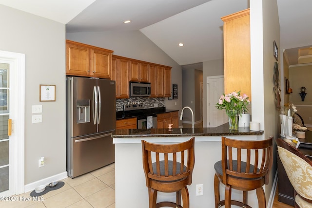 kitchen with decorative backsplash, a kitchen bar, vaulted ceiling, light tile patterned floors, and stainless steel appliances