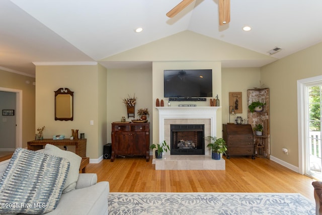 living area with ceiling fan, a fireplace, wood finished floors, vaulted ceiling, and visible vents