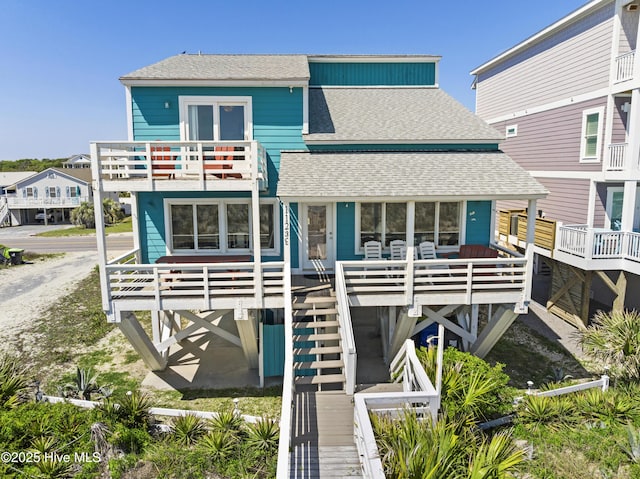rear view of property with stairway, a balcony, and roof with shingles
