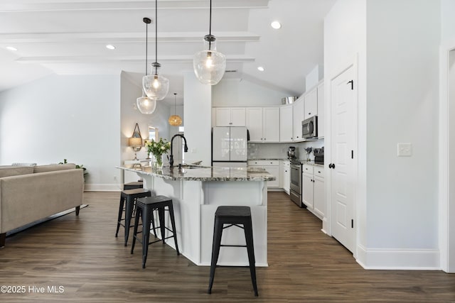kitchen with a kitchen breakfast bar, appliances with stainless steel finishes, a sink, baseboards, and vaulted ceiling with beams