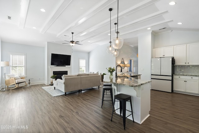 kitchen featuring freestanding refrigerator, a ceiling fan, light stone countertops, a kitchen breakfast bar, and a sink