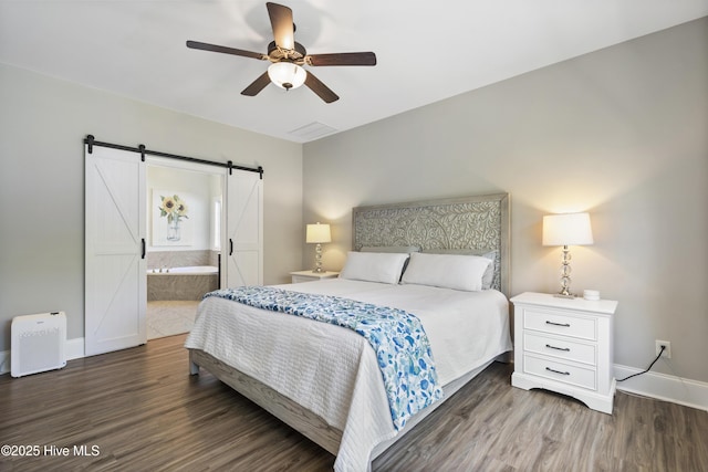 bedroom with baseboards, ensuite bath, a barn door, and wood finished floors