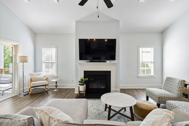 living area with a fireplace with flush hearth, baseboards, a ceiling fan, and wood finished floors
