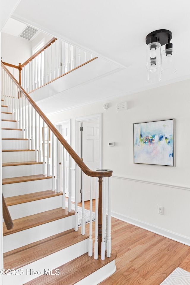 stairway featuring baseboards, wood finished floors, and visible vents