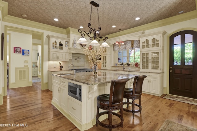 2220 Bel Arbor Pl, Wilmington, NC 28403 - kitchen featuring stainless steel microwave, a center island with sink, decorative backsplash, an ornate ceiling, and light stone countertops
