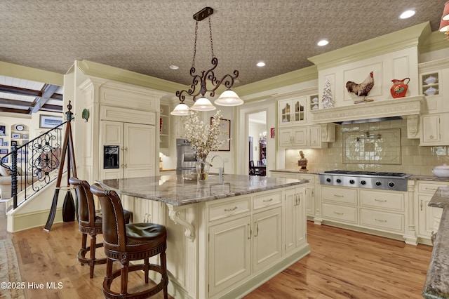 2220 Bel Arbor Pl, Wilmington, NC 28403 - kitchen featuring stainless steel gas stovetop, glass insert cabinets, light stone countertops, light wood-style floors, and a center island with sink