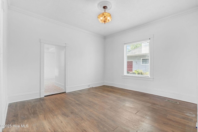 spare room with crown molding, baseboards, wood finished floors, and visible vents