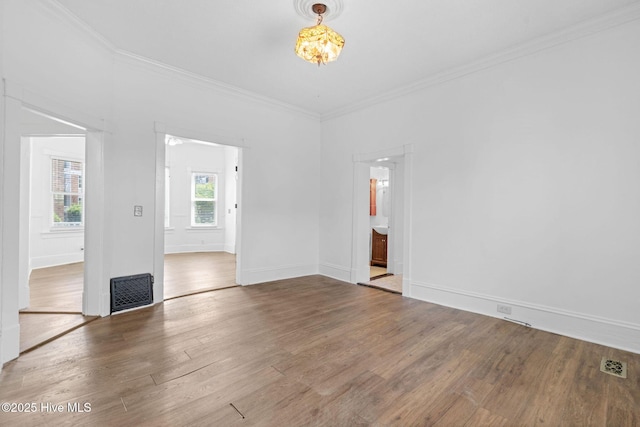 spare room with crown molding, baseboards, visible vents, and wood finished floors
