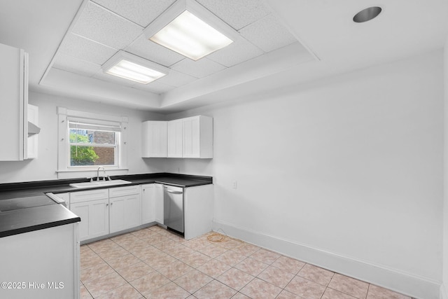 kitchen featuring stainless steel dishwasher, dark countertops, white cabinetry, a tray ceiling, and a sink