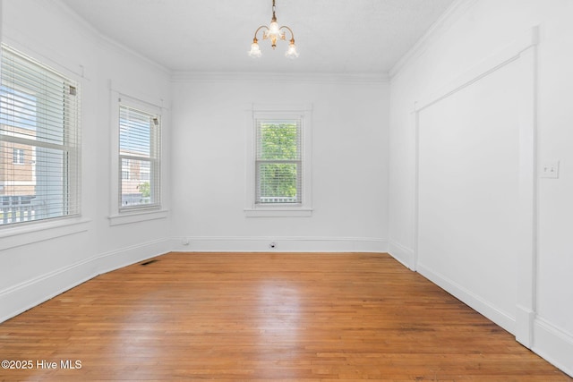 empty room featuring baseboards, a chandelier, ornamental molding, and light wood-style flooring