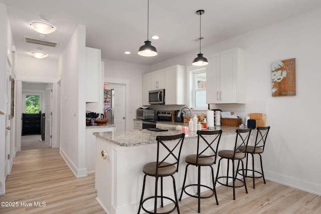 kitchen featuring white cabinets, light stone countertops, stainless steel appliances, a peninsula, and visible vents
