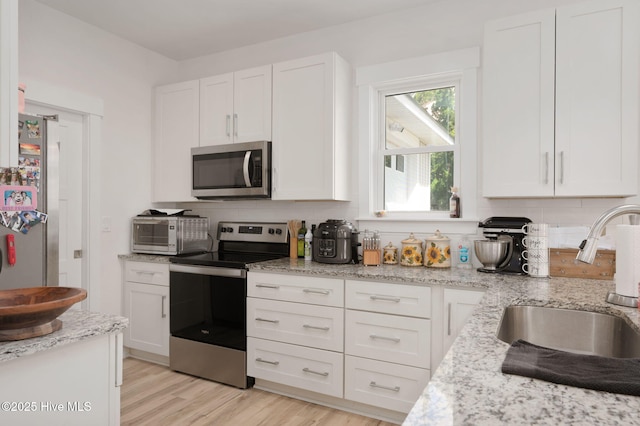 kitchen featuring appliances with stainless steel finishes, a sink, light wood-style floors, white cabinetry, and backsplash