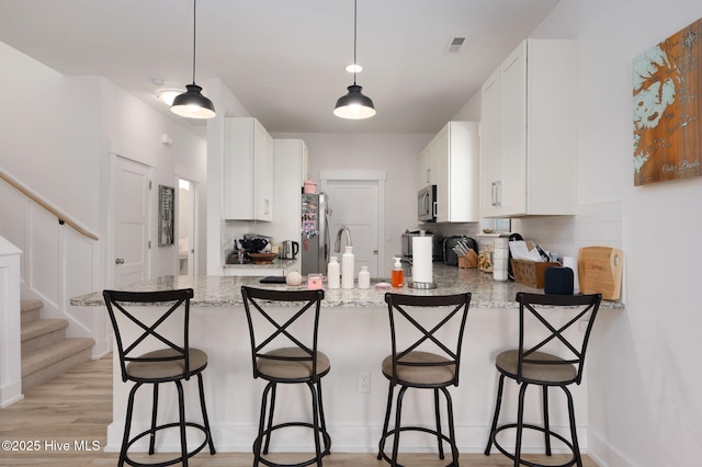 kitchen with appliances with stainless steel finishes, a peninsula, backsplash, and white cabinets