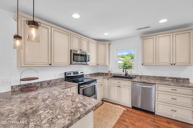 kitchen with appliances with stainless steel finishes, a sink, cream cabinetry, visible vents, and pendant lighting