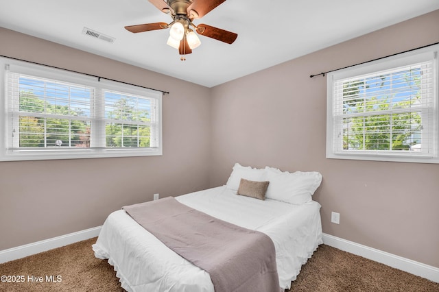 carpeted bedroom featuring baseboards, multiple windows, a ceiling fan, and visible vents
