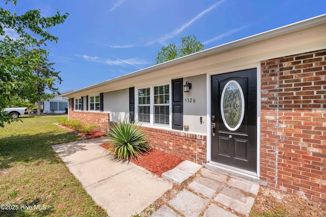doorway to property with a yard and brick siding