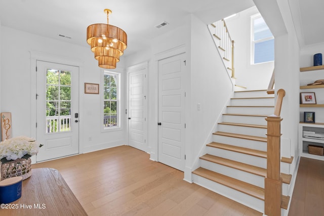 foyer entrance featuring an inviting chandelier, wood finished floors, visible vents, and stairway