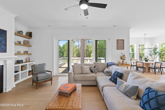 living area featuring a ceiling fan, light wood finished floors, a glass covered fireplace, and built in features