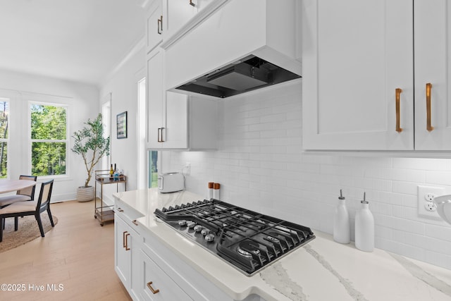 kitchen featuring decorative backsplash, stainless steel gas cooktop, premium range hood, white cabinets, and light stone counters