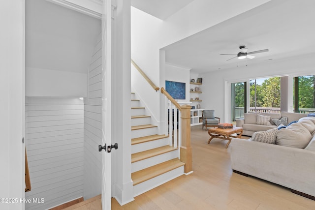 living room featuring light wood-style floors, ceiling fan, and stairs