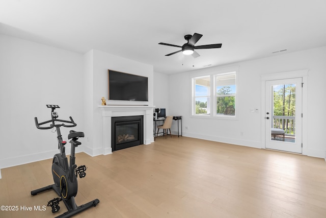 unfurnished living room with a glass covered fireplace, baseboards, a ceiling fan, and wood finished floors