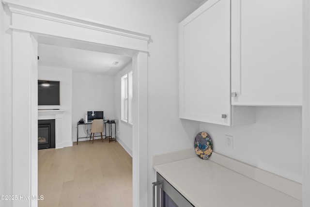 kitchen featuring light countertops, light wood finished floors, a glass covered fireplace, and white cabinets