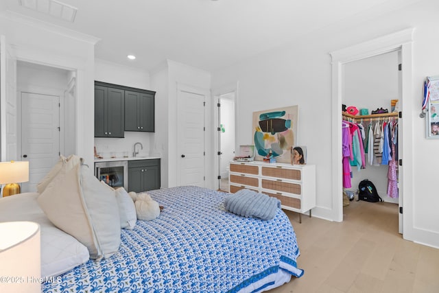 bedroom featuring visible vents, indoor wet bar, beverage cooler, a spacious closet, and light wood-style flooring