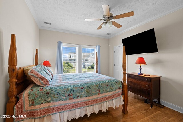 bedroom featuring wood finished floors, a textured ceiling, baseboards, a ceiling fan, and crown molding