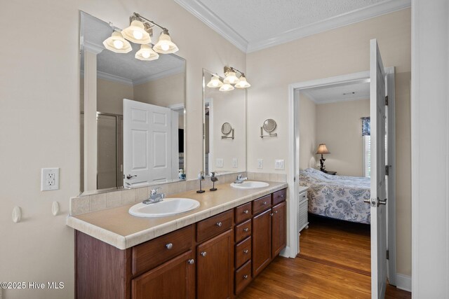 ensuite bathroom with wood finished floors, ornamental molding, double vanity, and a shower with shower door