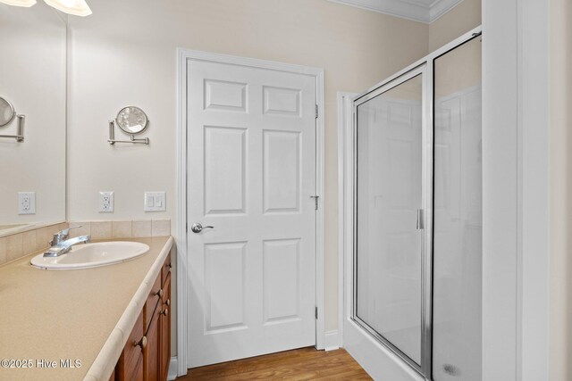 full bath featuring a stall shower, vanity, crown molding, and wood finished floors