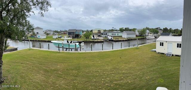 view of grassy yard with a water view, a residential view, and a boat dock
