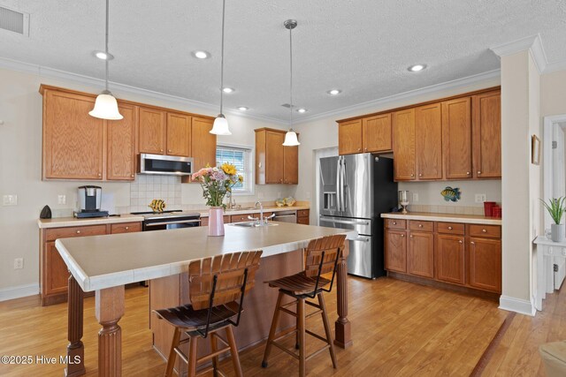 kitchen with appliances with stainless steel finishes, brown cabinetry, light wood-type flooring, crown molding, and a breakfast bar area