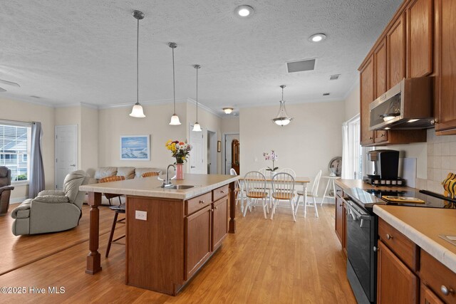 kitchen featuring range with electric stovetop, stainless steel microwave, open floor plan, brown cabinetry, and a sink