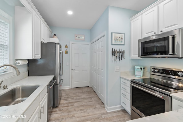 2403 W Oak Island Dr, Oak Island, NC 28465 - kitchen featuring appliances with stainless steel finishes, a sink, light wood-type flooring, white cabinetry, and baseboards