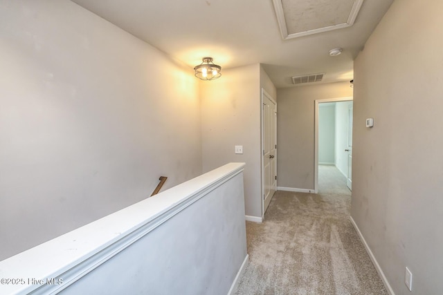 corridor featuring visible vents, attic access, baseboards, and light carpet