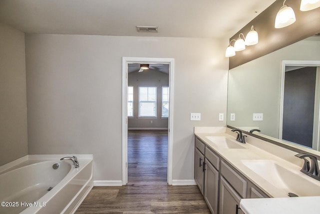 bathroom with a sink, a garden tub, wood finished floors, and visible vents