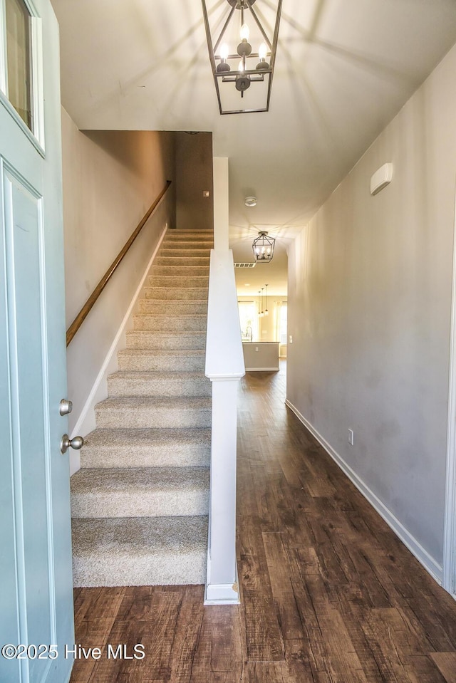 staircase featuring baseboards, a chandelier, and wood finished floors
