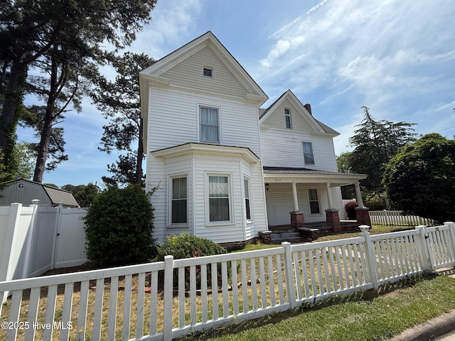 victorian home featuring a porch, a fenced backyard, a front lawn, and a chimney