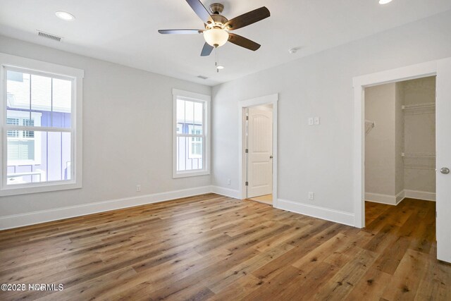 unfurnished bedroom with a walk in closet, multiple windows, wood finished floors, and visible vents