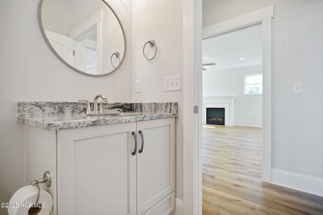 bathroom featuring vanity, wood finished floors, a fireplace, baseboards, and ceiling fan