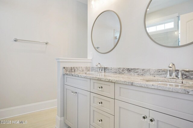 bathroom featuring double vanity, a sink, baseboards, and wood finished floors
