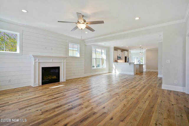 unfurnished living room with ceiling fan, crown molding, a glass covered fireplace, light wood-style floors, and recessed lighting