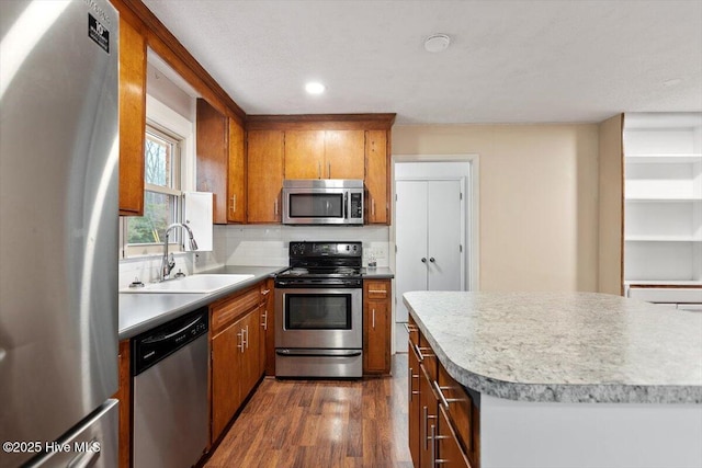 kitchen featuring brown cabinets, a sink, stainless steel appliances, recessed lighting, and dark wood-type flooring