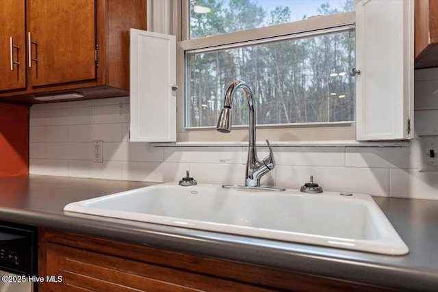 kitchen featuring brown cabinetry, decorative backsplash, dishwashing machine, white cabinets, and a sink