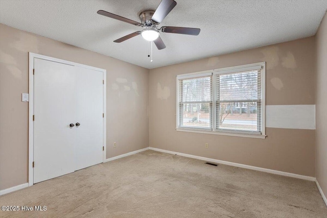 carpeted spare room featuring baseboards, a ceiling fan, a textured ceiling, and visible vents