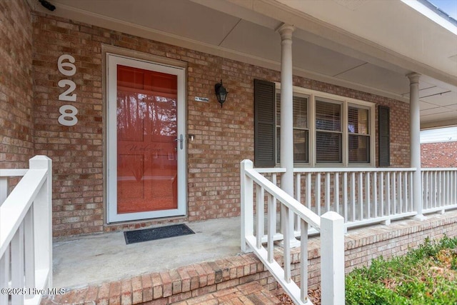 doorway to property featuring a porch and brick siding