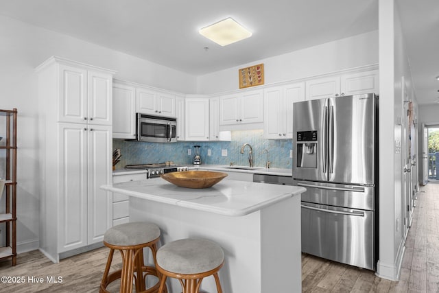 kitchen featuring stainless steel appliances, a sink, light wood-type flooring, white cabinets, and a center island