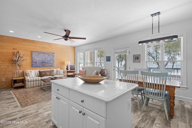 kitchen with light wood finished floors, a kitchen island, ceiling fan, white cabinetry, and wooden walls